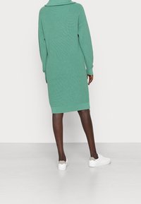 Robe en tricot vert menthe avec un large col, des manches longues et une coupe droite, associée à des baskets blanches. Le tissu texturé ajoute un intérêt visuel.