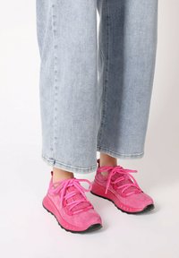 Helle rosa Sneakers aus Wildleder mit dicken Schnürsenkeln; Gummisohle; getragen mit hellblauen weiter geschnittenen Jeans.