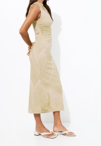 Robe ajustée jusqu'aux genoux en beige clair avec un col montant. Présente des détails froncés à la taille et un tissu lisse et extensible.