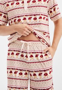 Korte mouwen pyjama set met een beige gegolfde stof en rode en crèmekleurige teddybeerpatronen. Inclusief een knoopsluiting bij de kraag en een tailleband met koord.