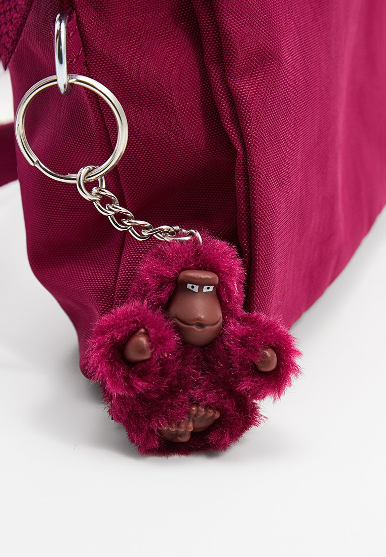 Borsa in tessuto fucsia con un portachiavi a catena argentata. Attaccata c'è una figura di scimmia pelosa color bordeaux con faccia e mani marroni, dotata di occhi bianchi.