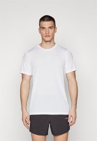Camiseta deportiva blanca de manga corta con textura acanalada, que presenta un logo azul sutil. Combinada con pantalones cortos oscuros.