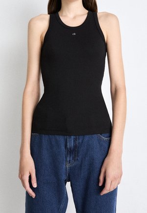 Czarny prążkowany top na ramiączkach z okrągłym dekoltem, z małym białym logo 'ck' na środku. Połączony z luźnymi niebieskimi dżinsami.