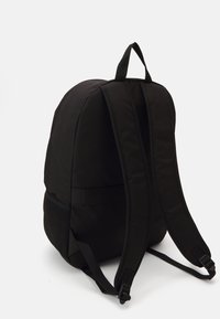 Mochila negra con un exterior de tela suave, diseño acolchado, correas ajustables y detalles de malla en los laterales. Sin marcas visibles.