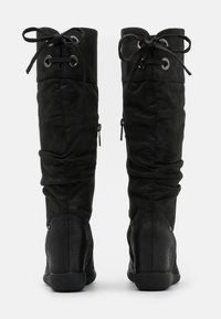 Paire de bottes noires montantes avec le haut replié et des lacets, vues de dos sur fond blanc.