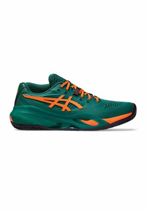 Grüner Sportschuh mit orangefarbenen Akzenten, orangen Schnürsenkeln und schwarzer Sohle, seitlich auf weißem Hintergrund gezeigt.