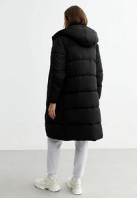 Svart puffjacka med huva, quiltad design, mellanhängig, bärs över gråa sweatpants och vita sneakers. Slätt, vattenavvisande material.