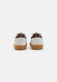 Baskets blanches avec une semelle en caoutchouc beige et un accent en imprimé léopard sur le talon. Tige en cuir lisse avec un bout arrondi et des lacets.