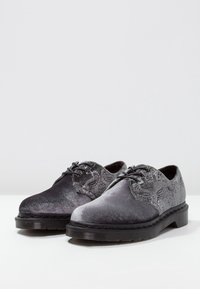 Chaussures noires et grises avec une surface texturée et des accents à motifs. Elles présentent un bout rond, des lacets et une semelle en caoutchouc durable.