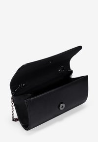 Bolso de mano de imitación cuero negro con cierre de botón a presión plateado y correa de cadena desmontable, con un exterior liso y un compartimento abierto.