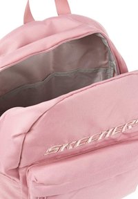 Mochila de tela rosa con un interior espacioso, que presenta un forro liso, bolsillos laterales y un logo bordado de “SKECHERS” en la parte frontal.