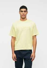 Geltona medvilninė marškinėliai su laisvu siluetu, apvaliu iškirpimu ir siuvinėtu "TOMMY JEANS" logotipu priekyje. Trumpomis rankovėmis, paprastas dizainas.