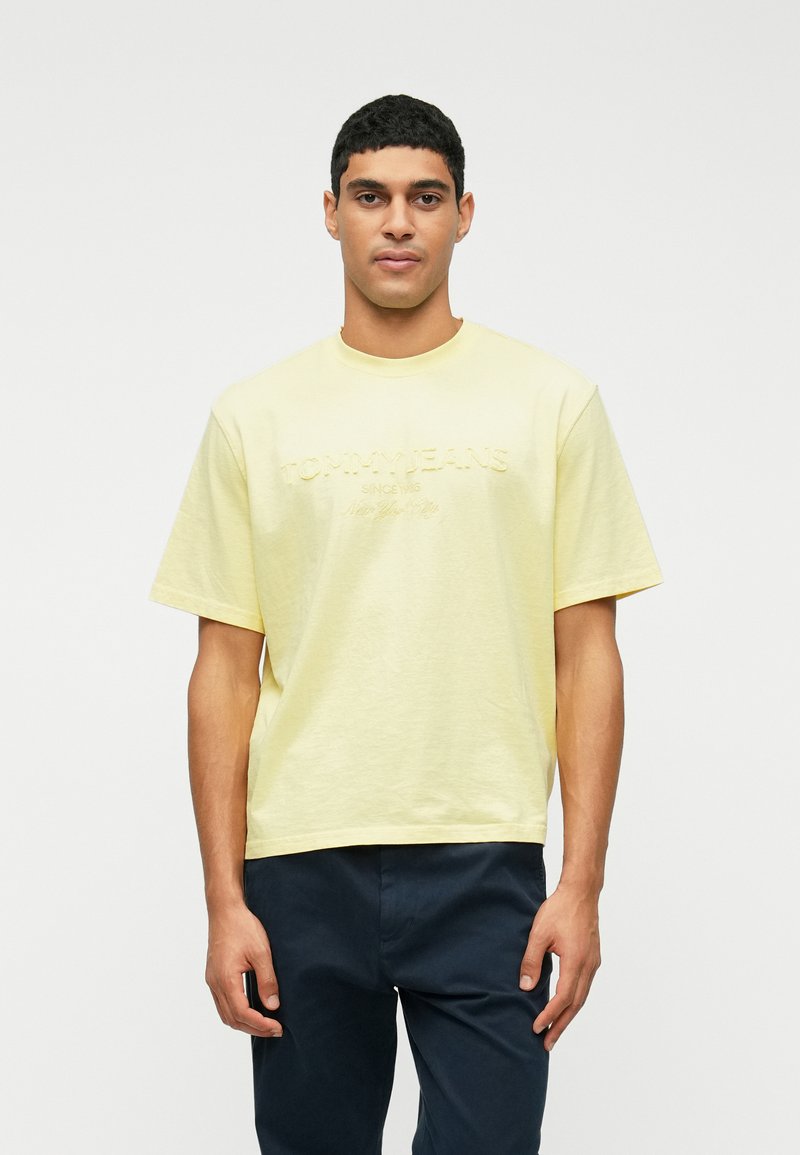 Geltona medvilninė marškinėliai su laisvu siluetu, apvaliu iškirpimu ir siuvinėtu "TOMMY JEANS" logotipu priekyje. Trumpomis rankovėmis, paprastas dizainas.