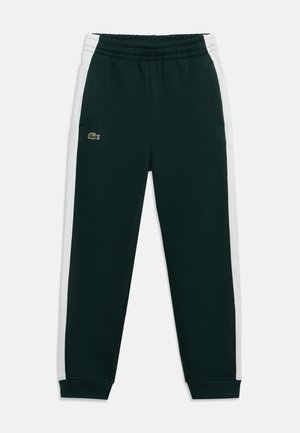 Pantalon de survêtement vert foncé avec bandes blanches sur les côtés, taille élastique, poignets et petit logo crocodile sur la cuisse gauche.