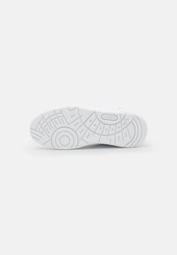 Semelle de sneaker en caoutchouc blanc avec des motifs texturés, présentant des motifs circulaires et linéaires, marquée du logo "LACOSTE".