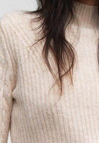 Pull en maille côtelée beige clair avec un col montant et un motif texturé, doté de fibres douces et d'une silhouette cintrée.