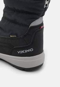 Botte noire imperméable avec un bas en caoutchouc texturé, des accents gris et un logo. Elle présente un haut rembourré et un label Gore-Tex pour l'isolation.