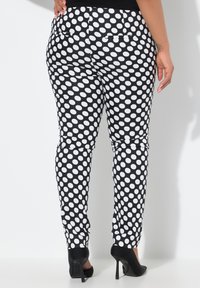 Zwart-witte polkadot stretchy broek met twee achterzakken, getailleerd ontwerp en taps toelopende pijpen, in combinatie met zwarte hoge hakken.