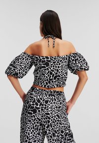 Zwart-witte cropped top met een off-the-shoulder ontwerp, ballonmouwen en een geometrisch patroon; heeft een striksluiting aan de achterkant.