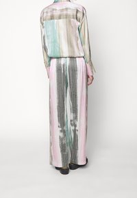 Barevný dvoudílný outfit skládající se z dlouhého rukávu košile a širokých kalhot se abstrahovanými liniovými vzory v zelených, růžových a šedých tónech.