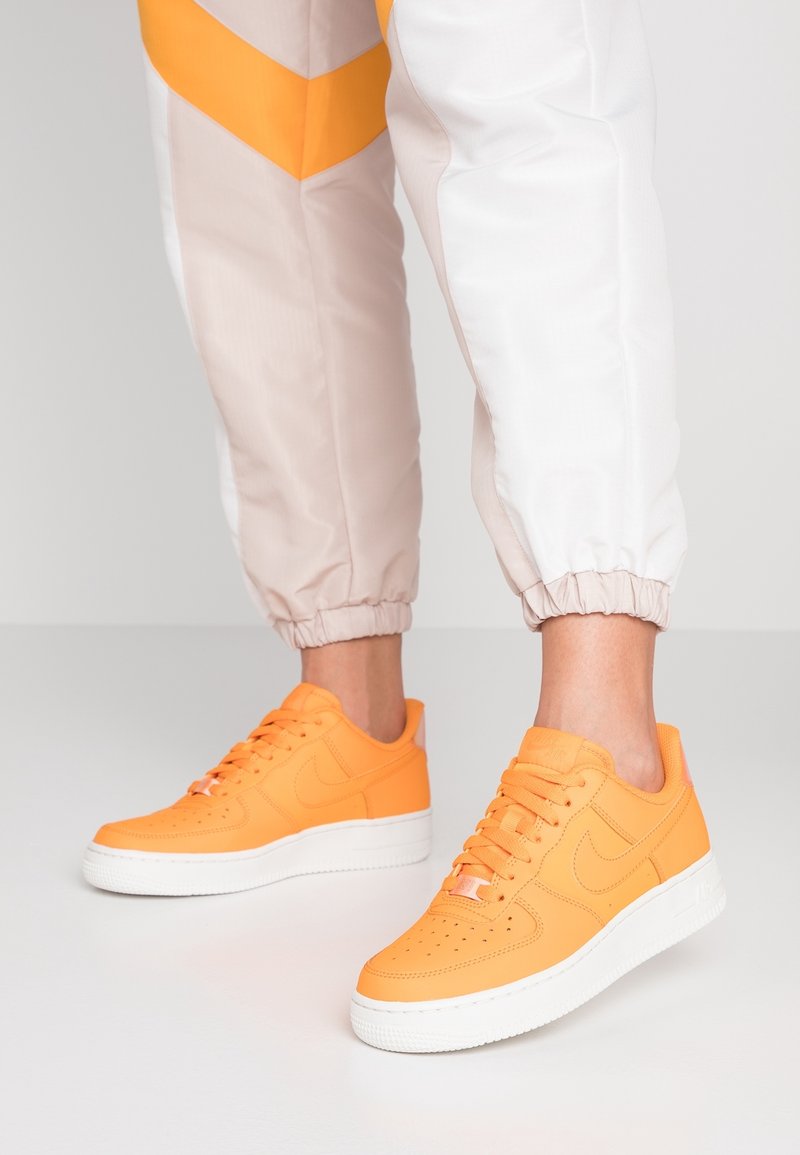 Baskets Nike Air Force 1 orange avec une tige en cuir lisse, des perforations sur le bout et une semelle en caoutchouc blanche.