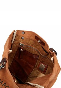 Binnenkant van een canvas tas in warm oranje-bruin met katoenen voering. Voorzien van een leren ritspocket, insteekvak en metalen studs. Inclusief gedetailleerd merketiket.