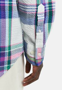 Camisa a cuadros con tejido texturizado en patrones morados, verdes y rosas. Mangas largas con cierres de botones y dobladillo en contraste.
