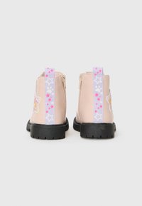 Bottes de cheville roses avec une sangle arrière à motif d'étoiles violettes et de jolis designs sur les côtés, présentées de dos sur un fond blanc.