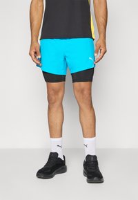 Herre aktive shorts i lys turkis med sort indre for, med logo-detalje og parret med sorte sneakers og hvide sokker.