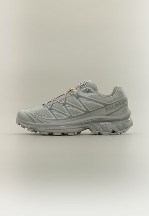 Zapatilla de trail running Salomon gris con suela texturizada y cordones multicolor sobre un fondo neutro, vista lateral.