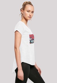 White T-shirt with a round neckline and short sleeves, featuring a graphic print of cartoon characters from "Stranger Things." Hem is slightly longer at the back.