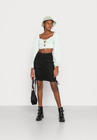 Top cropped em xadrez verde e branco com mangas bufantes, combinado com uma saia preta franzida e botas de combate pretas. Acessório: uma pequena bolsa preta.