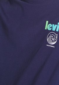 Tissu bleu avec le texte « levi's » en dégradé vert et bleu au-dessus d'un motif de vague blanche et le mot « CALIFORNIA » en dessous.