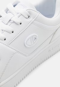 Białe sneakersy wykonane z gładkiego syntetycznego materiału. Posiadają perforowaną cholewkę, okrągłe sznurowadła oraz akcent z logo z boku. Teksturowana podeszwa.