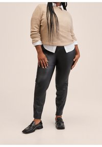 Světlý béžový svetr, pod ním bílá košile s límečkem, lesklé černé kalhoty z umělé kůže a černé mokasíny. Hladká textura se jemnými akcenty.