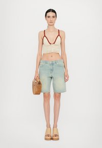 Kroširani bralet u krem boji s crvenim detaljima, u kombinaciji s svijetloplavim trapericama. Model drži torbicu od ispletenog drva i nosi svijetlosmeđe platforme.