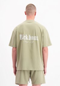 Olijfgroene katoenen t-shirt met een ronde hals en korte mouwen. Kenmerkt zich door een witte geborduurde logo op de achterkant, in combinatie met bijpassende shorts.