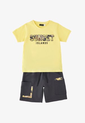 Żółta koszulka z krótkim rękawem z napisem „SUNSET ISLANDS” oraz ciemnoszare spodenki z bocznymi kieszeniami i żółtymi wzorzystymi akcentami.