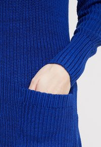 Dzianinowy sweter w jasnym niebieskim kolorze. Posiada ściągacze przy rękawach oraz boczną kieszeń z teksturowanym wzorem. Wykonany z miękkiej, lekkiej tkaniny.