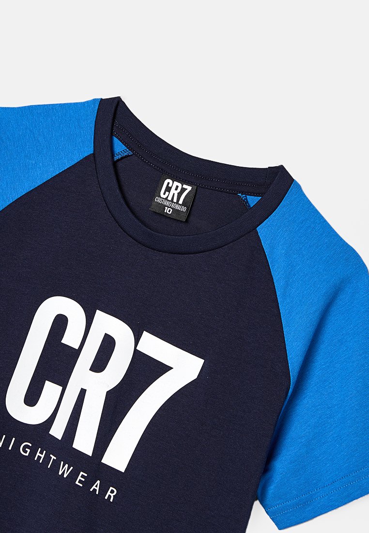 T-shirt bleu marine à manches courtes avec des manches raglan bleues, arborant un grand logo blanc "CR7 NIGHTWEAR" à l'avant. En tissu 100% coton.