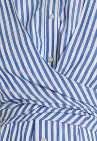 Niebiesko-biała tkanina w pionowe paski z guzikami, pokazująca złożoną i nachodzącą na siebie strukturę.