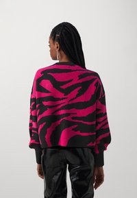 Överdimensionerad svart tröja med djärv rosa och svart zebrarandigt mönster. Har ribbade manschetter och fåll. Slät stickad struktur.