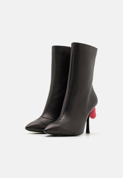 Black leather ankle boots with pointed toes and a high stiletto heel, featuring a unique red heart-shaped accent on the heel.