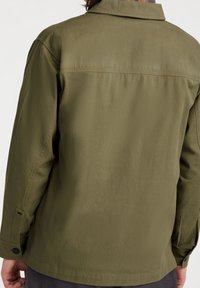 Olivově zelená, lehká bunda s límečkem, dlouhými rukávy a knoflíkovými manžetami. Hladký povrch s minimálně viditelnými švy.