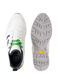 Chaussures de sport blanches avec des lacets verts, intérieur bleu marine, et semelle texturée détaillée avec un logo Vibram jaune sur fond blanc.