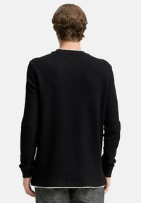 Schwarzer, langärmeliger, gerippter Pullover mit rundem Ausschnitt. Das Material ist strukturiert und zeichnet sich durch eine taillierte Silhouette sowie sichtbare Nahtdetails an den Bündchen aus.