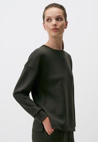 Donkergroene sweatshirt met een ontspannen pasvorm, ronde hals en lange mouwen. De stof lijkt soepel met ribgebreide manchetten en subtiele zijsplitten.