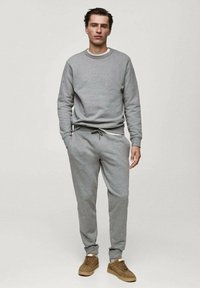 Hanorac gri cu guler rotund și manșete ribbed, asortat cu pantaloni jogger gri cu talie elastică. Adidași maro completează ținuta.