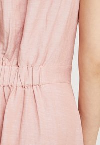 Ljusrosa klänning med en samlad midja, tillverkad av ett mjukt, texturerat tyg, med subtila färgvariationer och en slät yta.