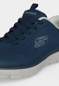 Baskets Skechers bleu marine avec dessus en mesh, fermeture à lacets, logo sur le côté, et semelle en caoutchouc blanche avec grip texturé.